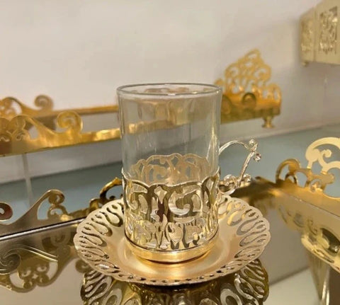 Glass tea cup with ornate gold metallic holder and saucer from luxury Arabic coffee sets.
