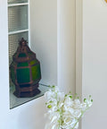 Decorative lantern on a shelf with a white flower arrangement in the foreground