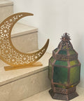 Decorative metal crescent moon and lantern with green glass on a stone surface