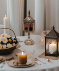 A metal lantern with multicolored glass windows, displaying a candle inside, placed on a table.