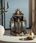 A distressed gold geometric lantern with engraved translucent glass displayed on a table, with decorative items in the background.