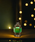 A bronze metal lantern with green glass panels, illuminated and set against a blurred background with bokeh lights.