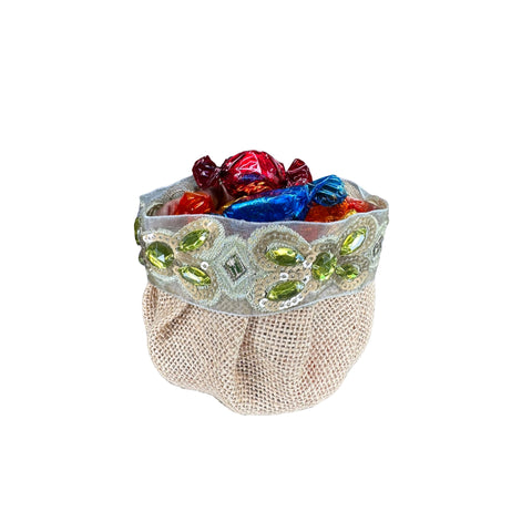A beige burlap candy pouch with blue and silver embroidered edges, filled with colorful candies.