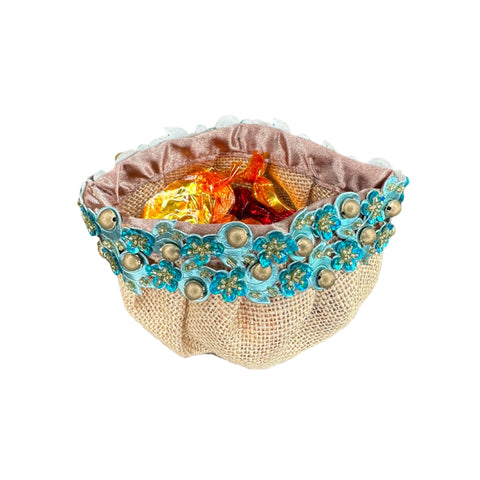 A beige burlap candy pouch with blue and silver embroidered edges, filled with colorful candies.