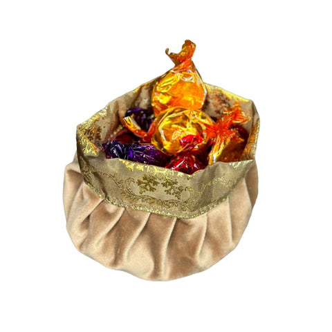 A beige velvet pouch with gold and multicolor floral embroidery, filled with colorful candy.
