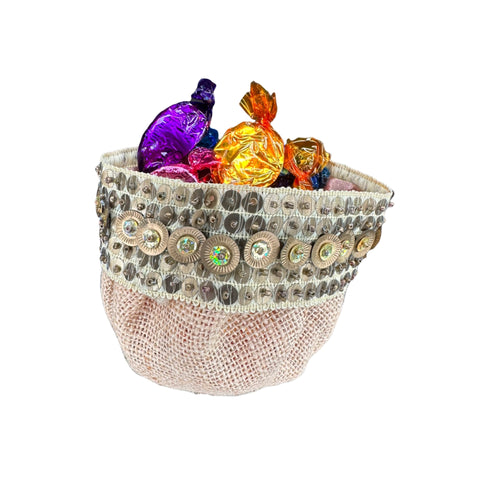 A beige burlap candy pouch with blue and silver embroidered edges, filled with colorful candies.