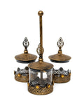 Three metal and glass jars connected with a vertical handle, used for serving different treats.
