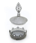 A glass jarr with metal id and with stons design in silver color on white background.