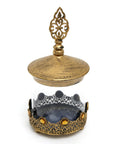 A glass jarr with metal id and with stons design in bronz color on white background.
